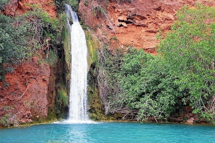 A waterfall cascading into a turquoise pool surrounded by red rock cliffs and green foliage. 1