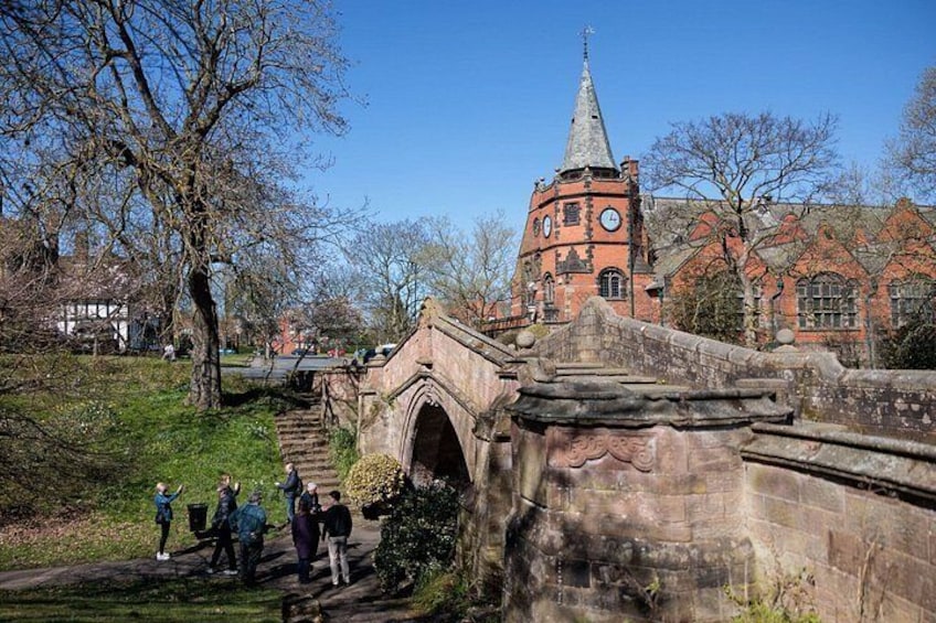 A stone bridge, a church with a spire, and a pathway with people walking. 5