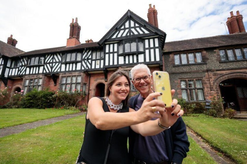 A historic Tudor-style building with a black and white facade, a central archway, and a well-maintained lawn. 3