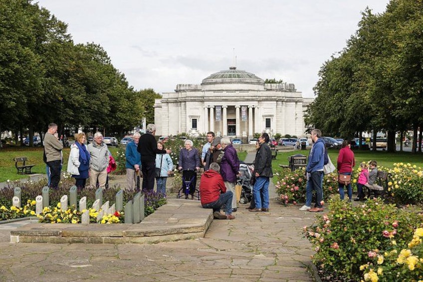 A group of people gathered in a park with a large building in the background. 2