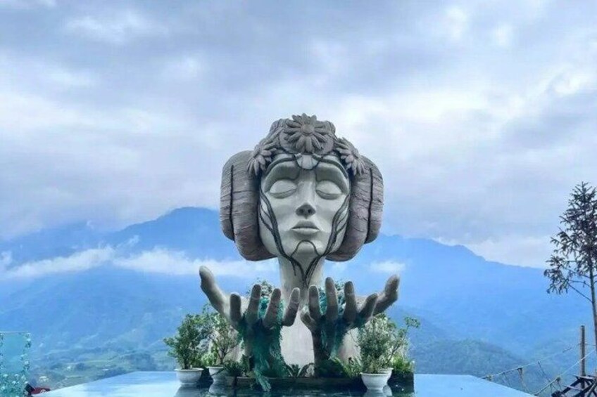 Una gran estatua de piedra con las manos levantadas, frente a un paisaje montañoso. 4