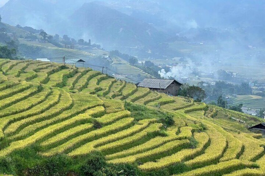 Terraced rice fields, a small house, and distant smoke from a chimney. 2