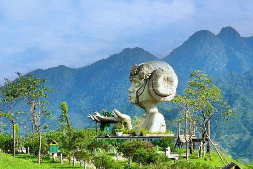Una gran escultura de piedra que representa la cabeza y los hombros de una mujer, rodeada de exuberante vegetación y montañas al fondo. 5