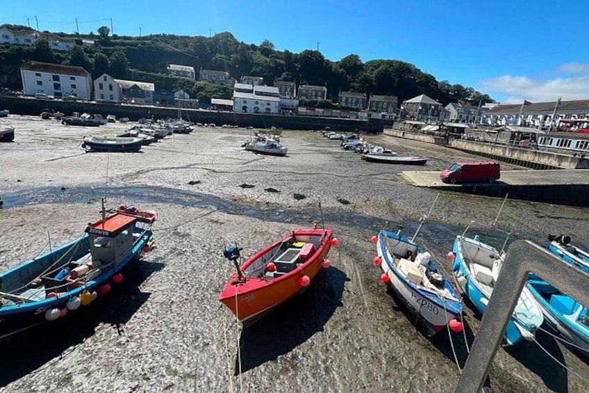 A harbor with boats docked on a pebbled shore, buildings in the background, and a clear sky. 3