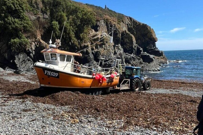 A boat named FH529 on a rocky beach with a tractor nearby. 4