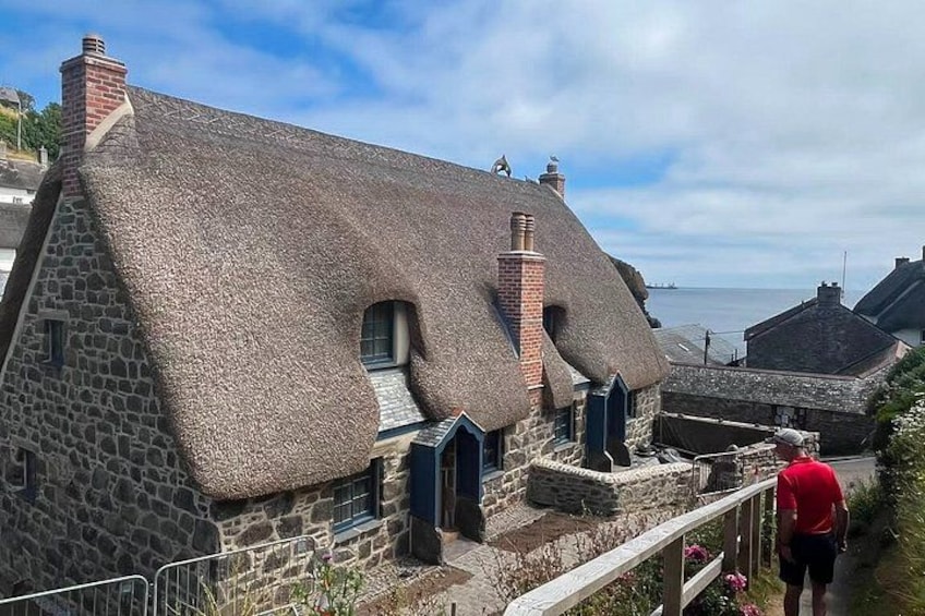 A stone house with a thatched roof, a wooden fence, and a person standing by the house. 4