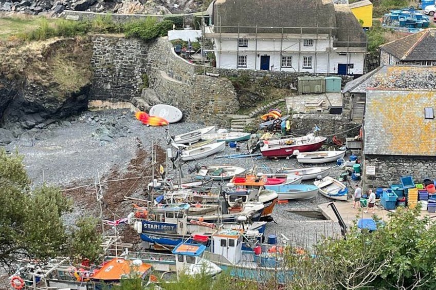 A coastal harbor with boats docked, a stone wall, and a building with a thatched roof. 1
