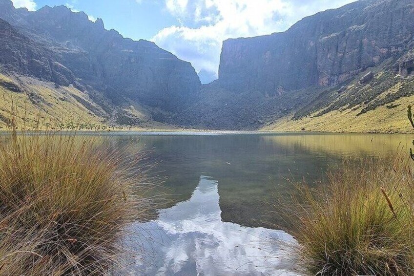 A calm lake surrounded by steep cliffs, with tall grasses in the foreground. 4