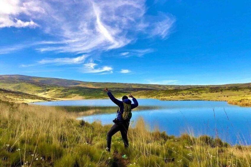 A person standing on a grassy hill overlooking a lake with a clear sky. 1