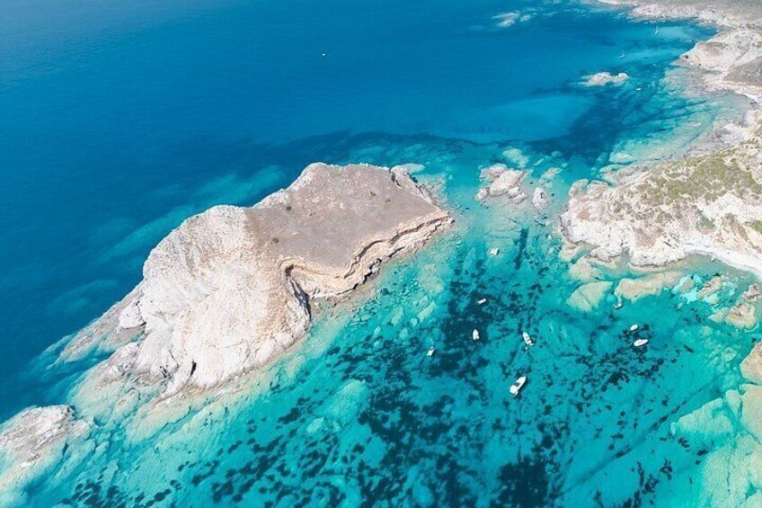 An aerial view of a coastal area with clear turquoise waters, a rocky outcrop, and several boats. 4