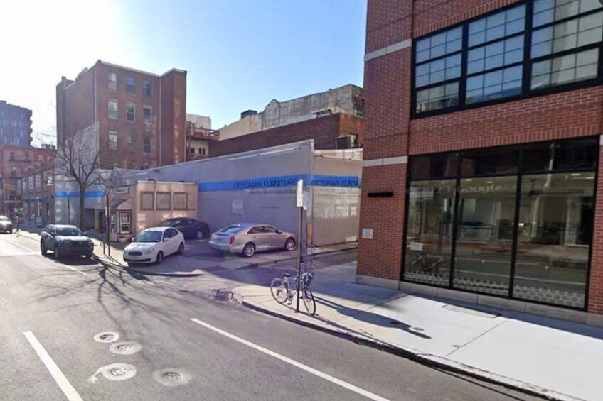 A street with parked cars, a bicycle, and a building with a blue sign. 1