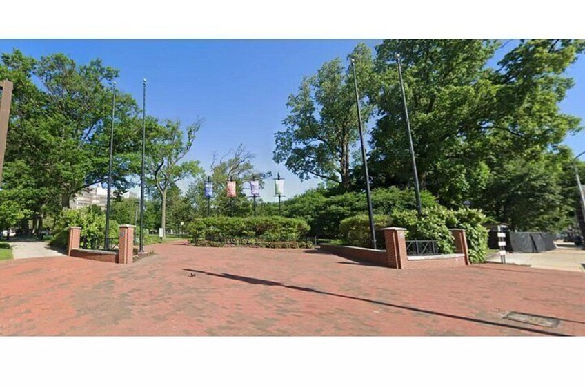 A paved entrance with brick pathways, surrounded by trees and a clear sky. 2