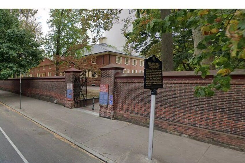 A brick wall with a gate, a signpost, and a building in the background. 4