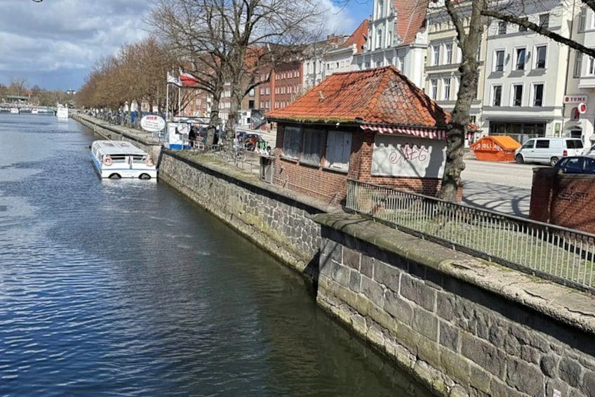 A canal with a boat, stone walls, and buildings with red roofs. 1
