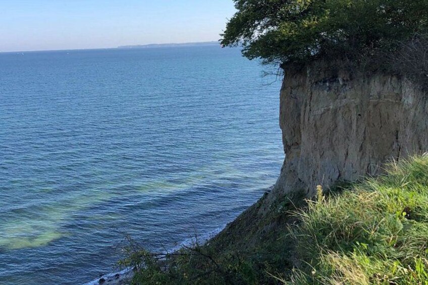 A coastal cliff with a grassy ledge and a clear view of the ocean. 2