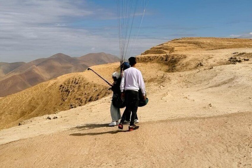 A person with a backpack and a child walking on a sandy path with mountains in the background. 2