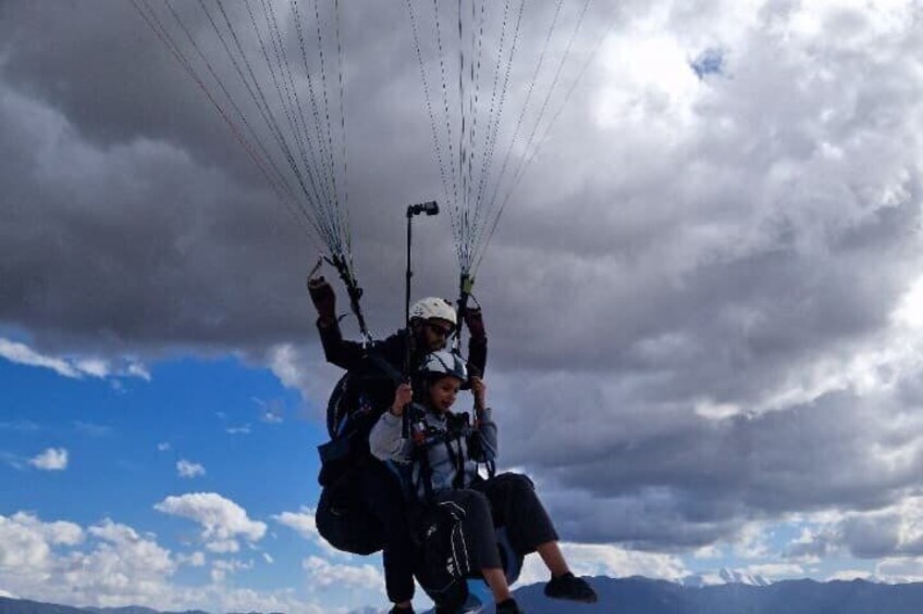 Two people paragliding with a mountainous landscape in the background. 2