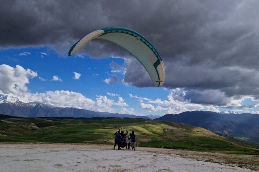 A person with a parachute on a grassy field with mountains in the background. 1