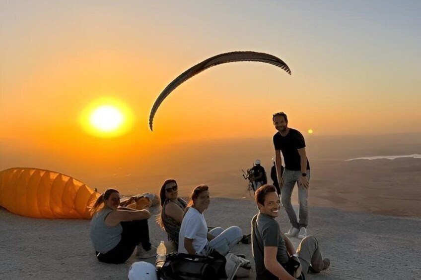 A group of people on a beach at sunset with a parachute. 4