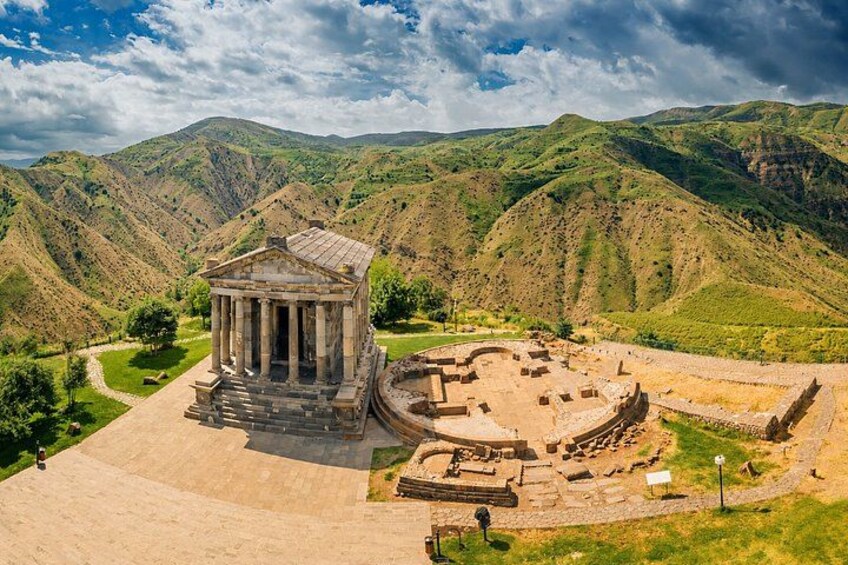 An ancient amphitheater with a temple in the foreground, surrounded by rolling hills. 3