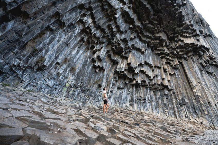 A person standing on a rocky surface with a large, textured cliff in the background. 5
