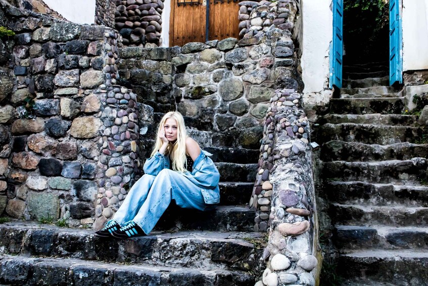 A person sitting on stone steps with a wooden door and blue shutters in the background. 2