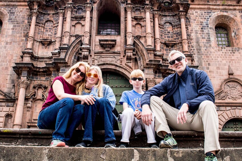 A group of people sitting on steps in front of a historic building with ornate architecture. 1
