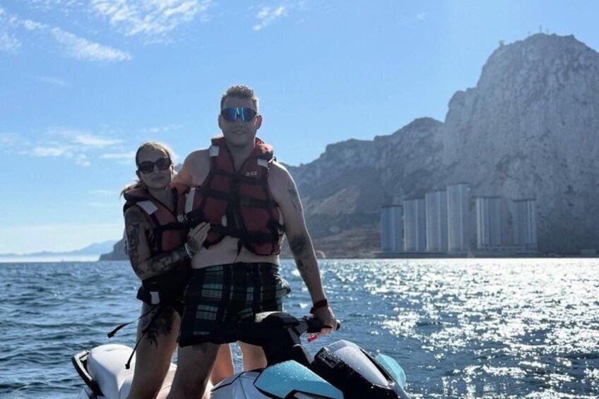 Two people on a jet ski with a mountainous coastline in the background. 3