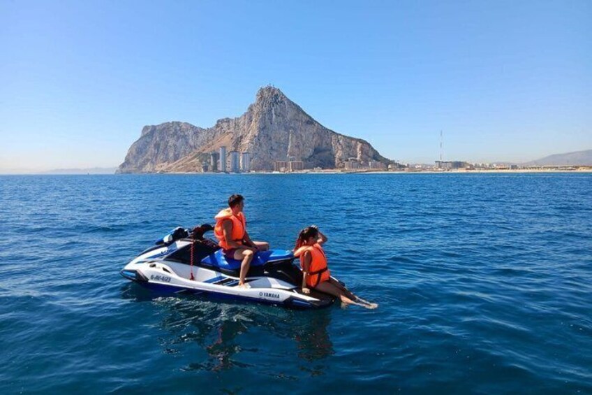 Two people on a jet ski in the water with a mountain in the background. 2