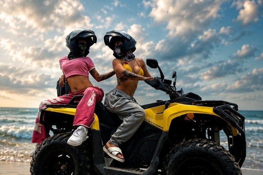 Two people on an ATV on a beach with the ocean in the background. 3