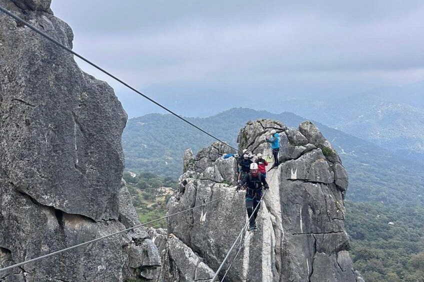 A group of people on a rope bridge over a rocky cliff with a mountainous landscape in the background. 2