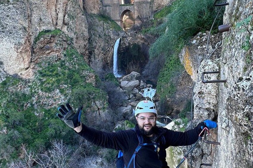 A person rappelling down a rocky cliff with a harness and helmet, surrounded by greenery and a waterfall in the background. 5