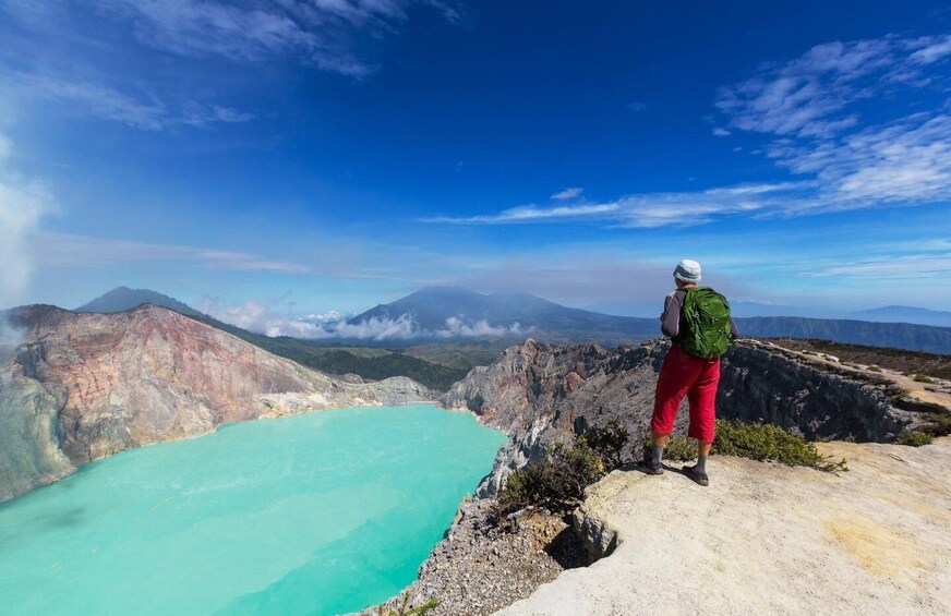 A hiker overlooking a turquoise lake surrounded by rugged mountains. 1