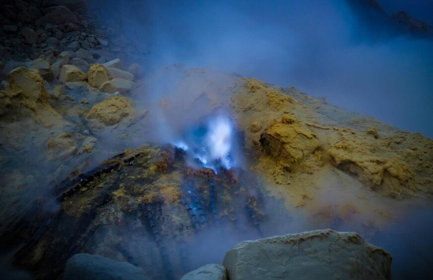 A geothermal area with steam rising from the ground, surrounded by rocks. 2