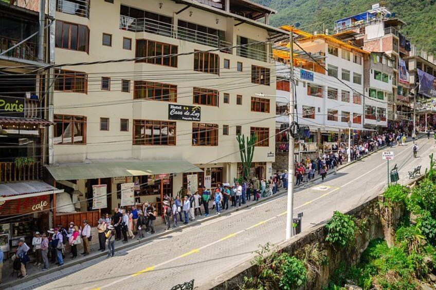 A street lined with buildings, a crowd of people, and a road with a drainage ditch. 4
