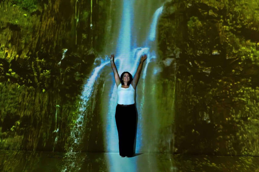 A person standing in front of a waterfall with arms raised. 5
