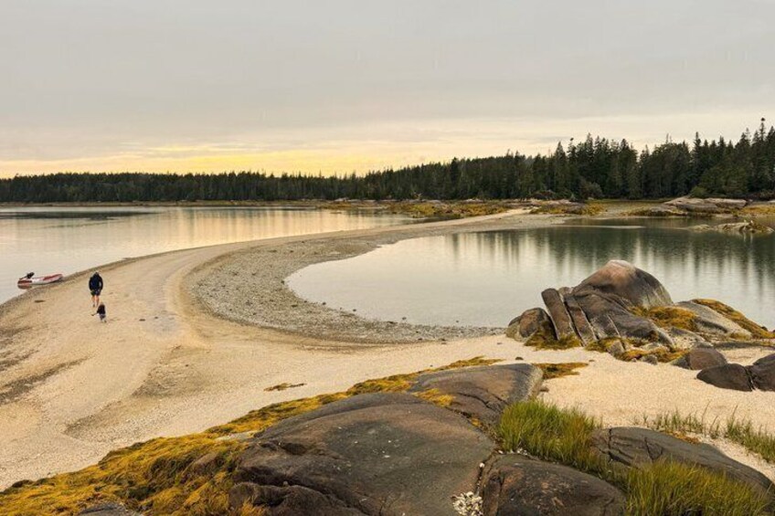 A calm lake with a person walking along the shore, surrounded by rocks and trees. 4