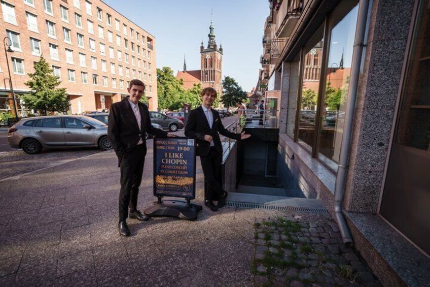 Two men standing in front of a building with a signboard. 3