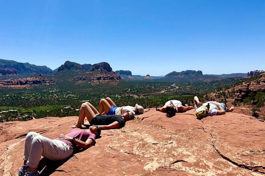 People lying on a red rock formation with a mountainous landscape in the background. 5