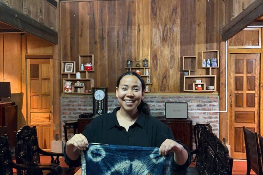 A person holding a blue and white patterned fabric in a rustic interior with wooden walls, shelves with various items, and a clock. 2