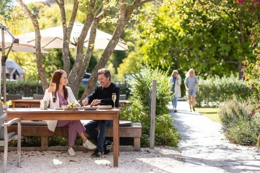 A couple dining at an outdoor table with a garden path in the background. 3