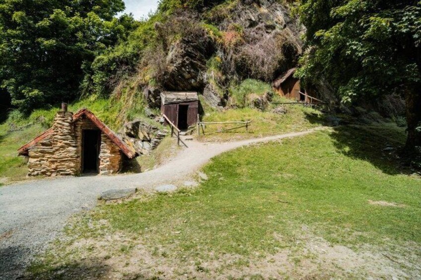 A stone building with a red roof, a wooden structure, and a dirt path leading uphill. 5