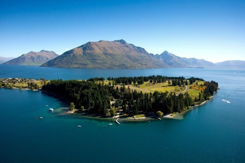 A lake surrounded by mountains, a forested island, and boats. 2