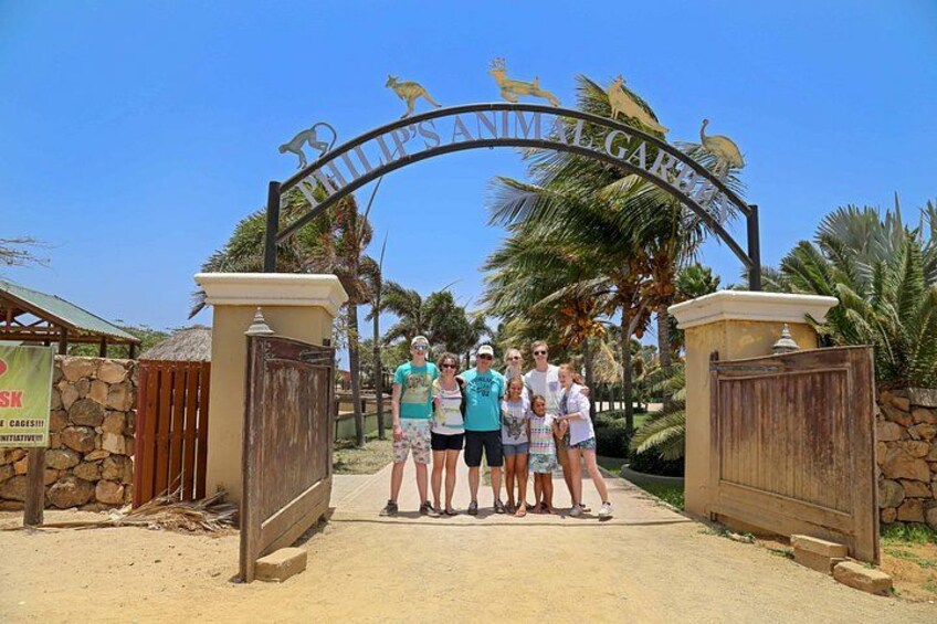 A group of people standing in front of a gate with a kangaroo and a sign that reads 'PHILIP'S ANIMAL GARDEN'. 1