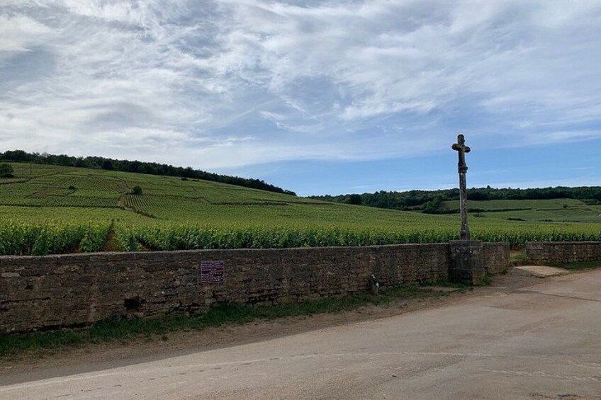A rural road with a stone wall and a cross on a post. 3