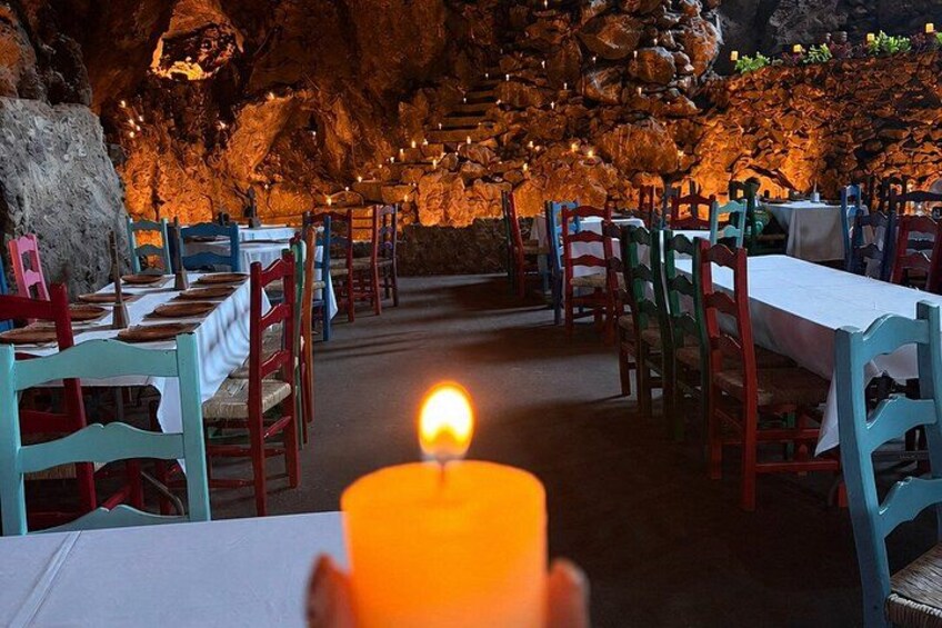 A candle-lit dining area with tables and chairs, set against a rocky cave background. 2