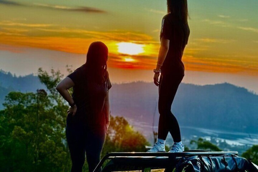 Two people standing on a vehicle with a sunset in the background. 1