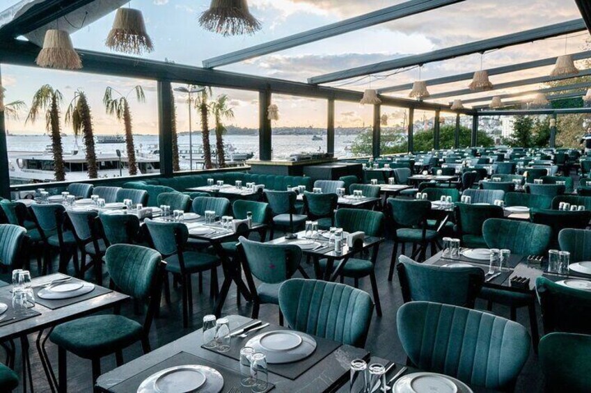 An outdoor restaurant with green chairs and tables, overlooking a body of water with palm trees. 5
