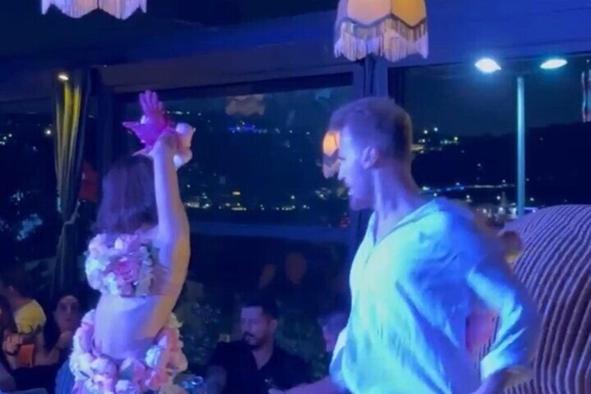 A person in a lei and a man in a light blue shirt at an indoor event with a cityscape in the background. 3