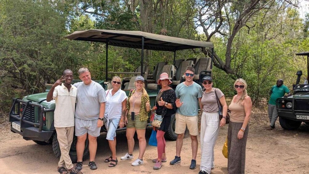 A group of people posing in front of a safari vehicle in a wooded area. 5